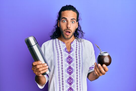 Young handsome man with long hair drinking mate infusion afraid and shocked with surprise and amazed expression, fear and excited face.