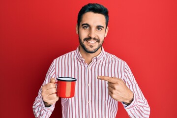 Young hispanic man holding coffee smiling happy pointing with hand and finger