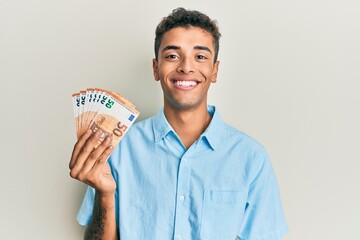 Young handsome african american man holding bunch of 50 euro banknotes looking positive and happy...