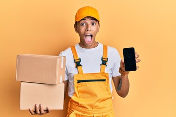 Young handsome african american man holding delivery package and showing smartphone screen celebrating crazy and amazed for success with open eyes screaming excited.