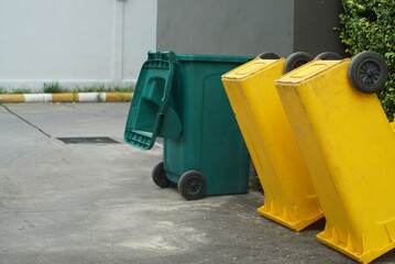 A yellow and green trash of beside a building on the road.