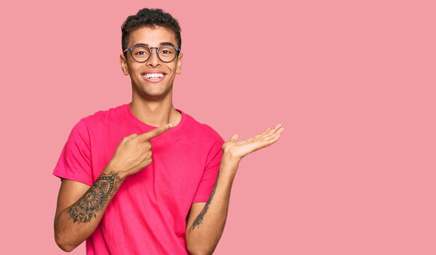 Young handsome african american man wearing casual clothes amazed and smiling to the camera while presenting with hand and pointing with finger.