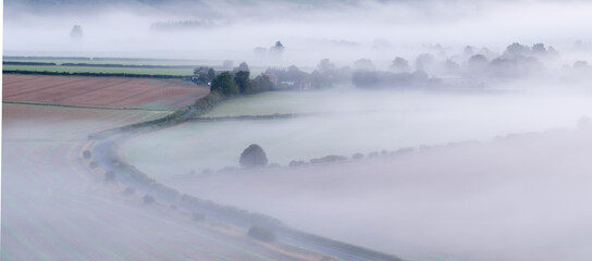 A misty morning in the South Downs National Park in Hampshire. Shows a road curving into the mist near East Meon with farmers fields either side.
