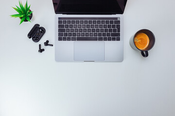 Top view of gray laptop with coffee cup, small plant and wifi earphones on white background - Powered by Adobe