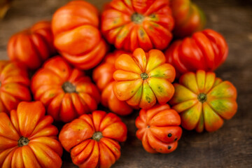 Obraz premium Red ribbed tomatoes on a wooden background. American or Florentine variety Nina. Food on the table top view. Autumn harvest of vegetables similar to flowers and pumpkins.Ribby tomato.