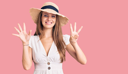 Young beautiful blonde woman wearing summer dress and hat showing and pointing up with fingers number eight while smiling confident and happy.