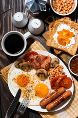 Fried eggs with bacon, sausages and vegetables, vertical top view