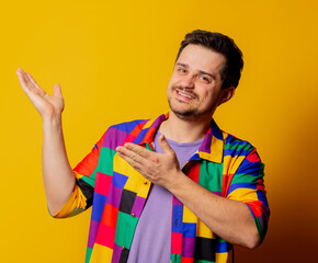 smiling guy in 90s shirt points with hands on yellow background