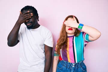 Interracial couple wearing casual clothes covering eyes with hand, looking serious and sad. sightless, hiding and rejection concept