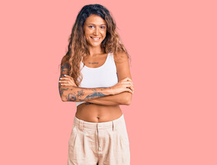 Young hispanic woman with tattoo wearing casual clothes happy face smiling with crossed arms looking at the camera. positive person.