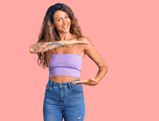 Young hispanic woman with tattoo wearing casual clothes gesturing with hands showing big and large size sign, measure symbol. smiling looking at the camera. measuring concept.