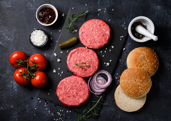 Obraz na płótnie Canvas Raw ground beef meat burger steak cutlets with salt, rosemary, bun and tomatoes on dark background