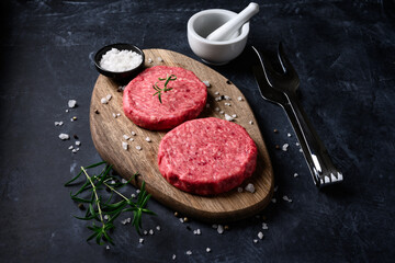 Raw ground beef meat burger steak cutlets with salt and rosemary on dark background