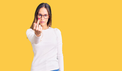 Beautiful brunette young woman wearing casual white sweater and glasses showing middle finger, impolite and rude fuck off expression