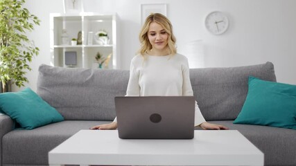 Happy young woman with blond hair waving and talking during video chat on laptop. Pretty female sitting on couch and having conference on computer.