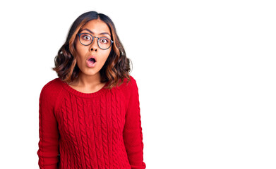 Young beautiful mixed race woman wearing red sweater and glasses scared and amazed with open mouth for surprise, disbelief face