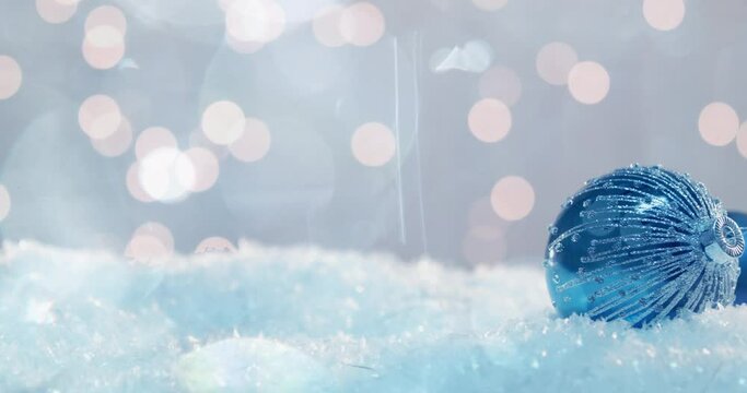 A shiny glass christmas ornaments with a pattern of thin silver stripes lying in drifts of artificial snow
