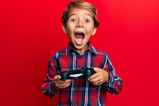 Adorable latin kid playing video game holding controller celebrating crazy and amazed for success with open eyes screaming excited.