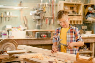 Young boy hammering a nail in wooden plank in  carpentry workshop