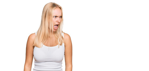 Young blonde girl wearing casual style with sleeveless shirt angry and mad screaming frustrated and...