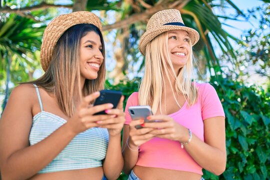 Two beautiful and young girl friends together having fun at the city using smartphone