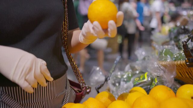 close up female hand wearing protective rubber glove choosing fresh fruit orange in supermarket new normal lifestyle