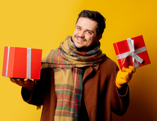 Style man in coat and scarf with gift box on yellow background