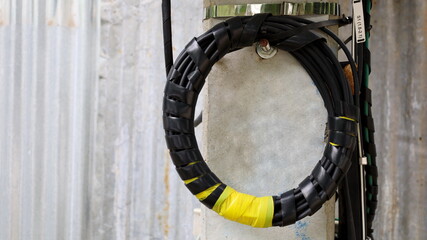 A roll of fiber-optic cables hanging from a pole. Optical fiber cable of high speed internet communication On the background of a galvanized wall with a copy area. Close focus and select an object