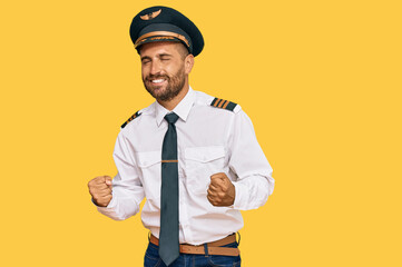 Handsome man with beard wearing airplane pilot uniform very happy and excited doing winner gesture with arms raised, smiling and screaming for success. celebration concept.