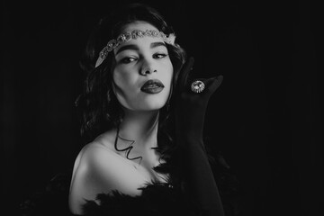 Black and white portrait of lady dressed in roaring twenties era with feathers boa on dark background. Retro, party, fashion concept. Sepia film effect.