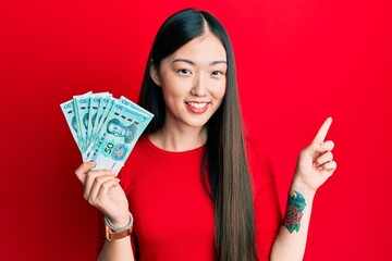 Young chinese woman holding 50 yuan chinese banknotes smiling happy pointing with hand and finger to the side