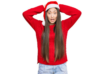 Young chinese woman wearing christmas hat crazy and scared with hands on head, afraid and surprised of shock with open mouth