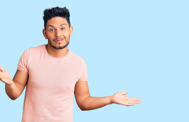 Handsome latin american young man wearing casual clothes clueless and confused expression with arms...