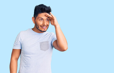 Handsome latin american young man wearing casual clothes very happy and smiling looking far away with hand over head. searching concept.