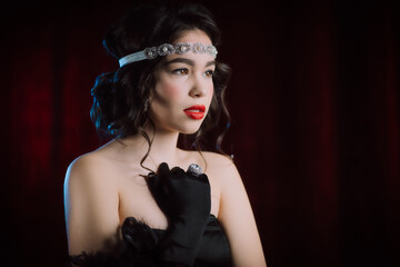 Old-fashioned woman dressed in style of Flappers posing on dark red background. Roaring twenties,...