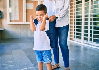 Adorable latin student boy and mom at school. Mother preparing kid putting up backpack.