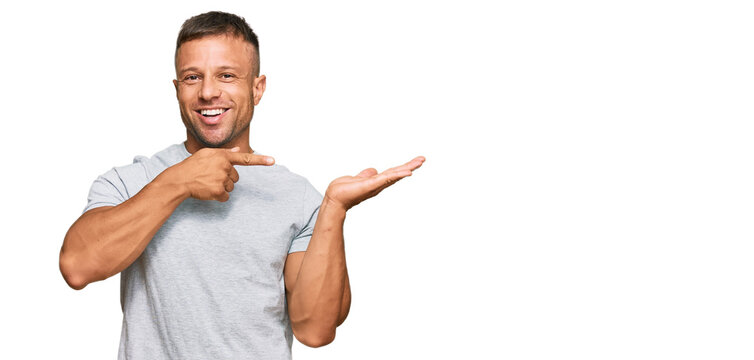 Handsome muscle man wearing casual grey tshirt amazed and smiling to the camera while presenting with hand and pointing with finger.