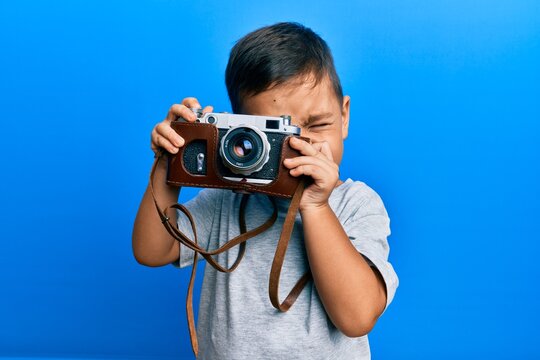 Adorable latin photographer toddler smiling happy using vintage camera over isolated blue background.