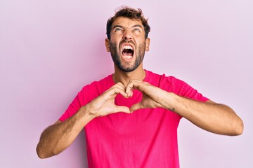 Handsome man with beard making heart symbol with hands shape angry and mad screaming frustrated and furious, shouting with anger looking up.