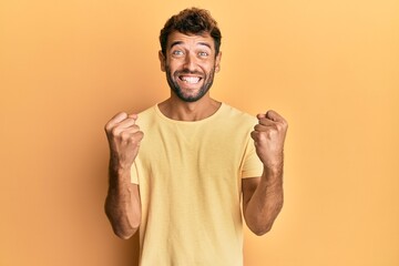 Fototapeta premium Handsome man with beard wearing casual yellow tshirt over yellow background celebrating surprised and amazed for success with arms raised and open eyes. winner concept.