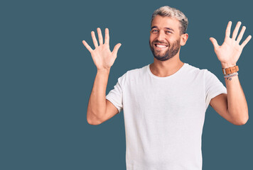 Naklejka premium Young handsome blond man wearing casual t-shirt showing and pointing up with fingers number ten while smiling confident and happy.