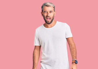 Young handsome blond man wearing casual t-shirt winking looking at the camera with sexy expression, cheerful and happy face.