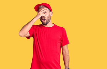 Fototapeta premium Young handsome blond man wearing t-shirt and cap peeking in shock covering face and eyes with hand, looking through fingers with embarrassed expression.