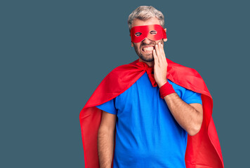 Young blond man wearing super hero custome touching mouth with hand with painful expression because of toothache or dental illness on teeth. dentist