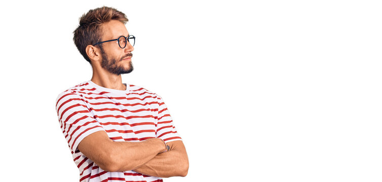 Handsome blond man with beard wearing casual clothes and glasses looking to the side with arms crossed convinced and confident