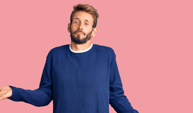 Handsome blond man with beard wearing casual sweater clueless and confused expression with arms and hands raised. doubt concept.