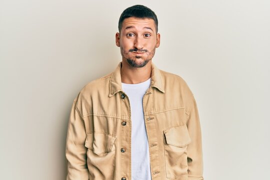 Handsome man with tattoos wearing casual brown denim jacket puffing cheeks with funny face. mouth inflated with air, crazy expression.