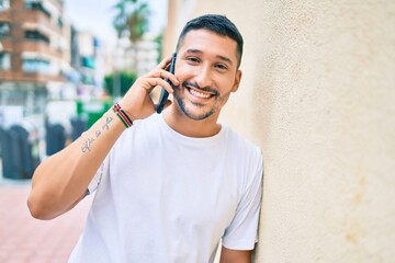 Young hispanic man smiling happy talking on the smartphone leaning on the wall.