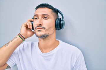 Young hispanic man smiling happy listening to music using headphones at street of city.