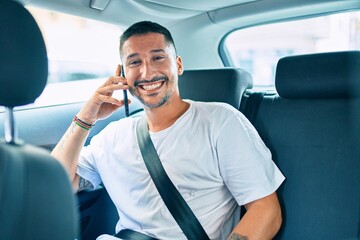 Young hispanic man smiling happy talking on the smartphone sitting on the car.